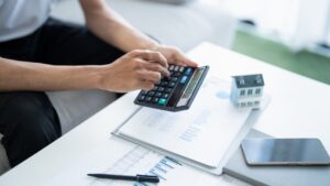 Persona usando una calculadora en una mesa con documentos y una casa en miniatura
