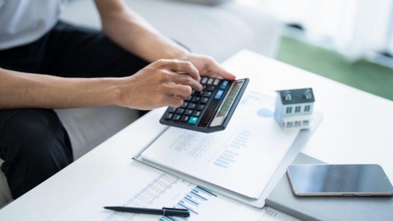 Persona usando una calculadora en una mesa con documentos y una casa en miniatura
